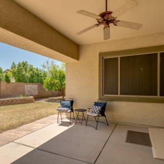 A covered patio with seating and a ceiling fan overlooks a backyard.