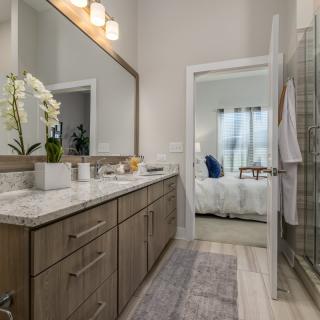 A modern bathroom featuring a large vanity with a mirror, elegant lighting, and a glass-enclosed shower.