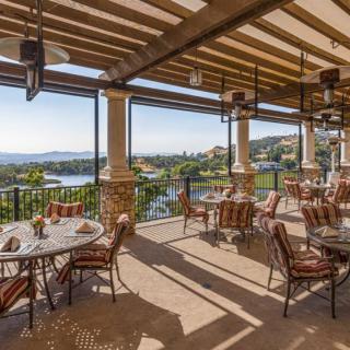 A beautifully arranged outdoor dining area with panoramic views of a lake and surrounding landscape.