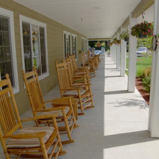 A row of wooden rocking chairs on a sunny porch.
