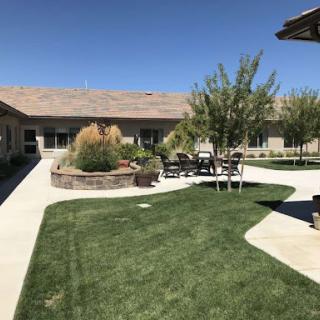 A serene courtyard featuring well-maintained grass, trees, and outdoor seating under a clear blue sky.