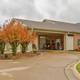 A building entrance with a driveway and autumn-colored trees under a cloudy sky.