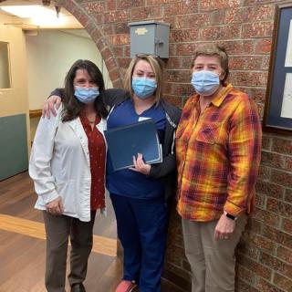 Three individuals wearing masks, standing together indoors in a hallway.