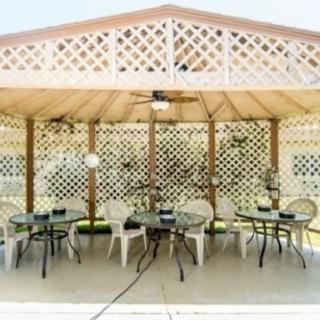 An outdoor patio area featuring a gazebo with tables and chairs arranged neatly under a lattice roof and a ceiling fan.