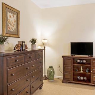 A cozy bedroom with dark wood furniture, including a dresser and TV stand, plemented by decorative items and a floor lamp.