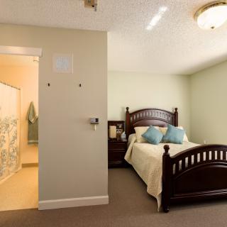 A cozy bedroom with a wooden bed and nightstand, adjacent to a bathroom.