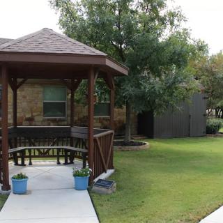 A wooden gazebo in a well-maintained garden setting with lush green grass and trees.