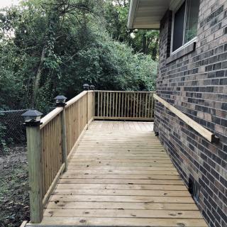 A wooden deck with railings adjacent to a brick house, overlooking a lush backyard.