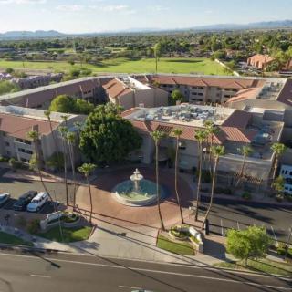 Aerial view of a building complex surrounded by palm trees and featuring a central fountain.