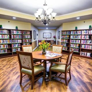 A cozy library with a round table and chairs, surrounded by bookshelves and illuminated by a chandelier.