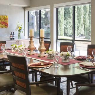 A beautifully set dining room table with candles and floral arrangements near large windows.