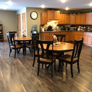 A cozy kitchen and dining area with wood flooring, featuring two round tables and accompanying chairs, set against a backdrop of wooden cabinets.