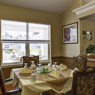 A cozy dining room with a neatly set table, featuring elegant decor and a large window allowing natural light to brighten the space.