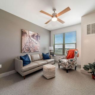 A cozy living room with a sofa, armchair, and ceiling fan in a bright space.