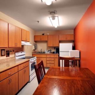 A cozy kitchen featuring wooden cabinetry, modern appliances, and a warm orange accent wall.
