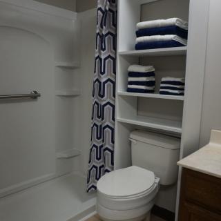 A modern bathroom with a shower, toilet, and neatly stored towels on shelves.