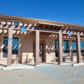 A modern commercial building featuring a pergola and large windows under a clear blue sky.