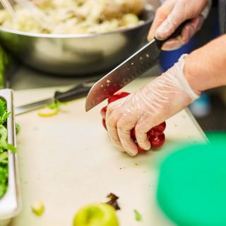 A person wearing gloves chops vegetables with a knife in a kitchen.