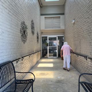 An elderly person walking towards the entrance of a well-lit hallway with benches on either side.
