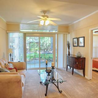 A cozy living room with a sofa, glass coffee table, and ceiling fan, featuring sliding doors that let in natural light.