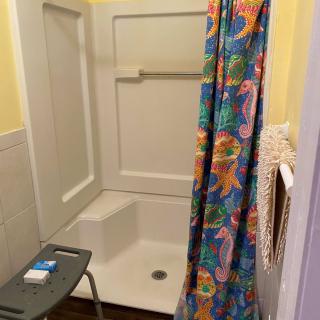 A bathroom with a colorful shower curtain and a safety chair.
