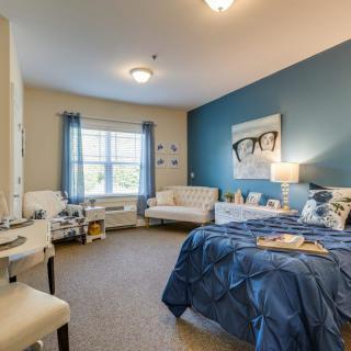 A cozy and well-decorated bedroom with blue accents, featuring a bed, sofa, and ample natural light.