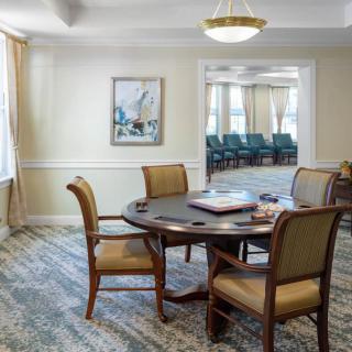 A cozy dining room with a round table and four chairs, featuring a carpeted floor, artwork on the wall, and warm lighting.