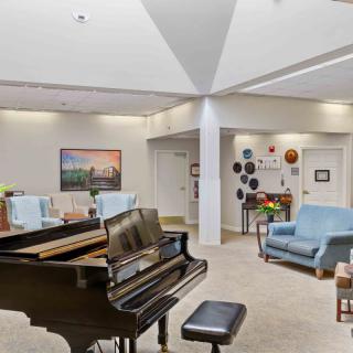 A spacious living room with a grand piano, comfortable seating, and decorative artwork.