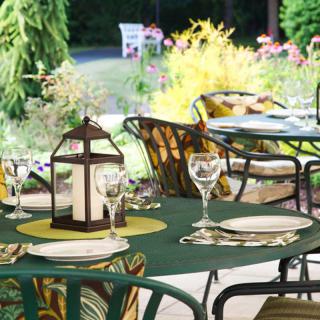 An inviting outdoor dining setup featuring tables with elegant place settings and lanterns, surrounded by lush greenery.