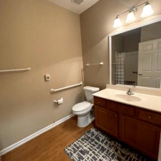 A well-lit bathroom with a vanity, sink, and toilet on hardwood flooring.