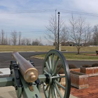 A historic cannon displayed in an outdoor setting, surrounded by trees and open grass.