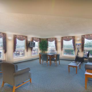 A spacious lounge area with multiple windows, decorated with comfortable seating and tables.