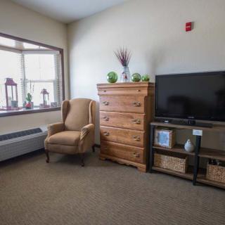 A cozy living room with an armchair, wooden cabinet, and television by a large window.