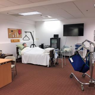A hospital room with a mannequin in a bed and various medical equipment.