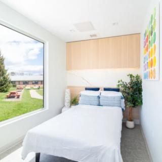 A minimalist bedroom with a large window offering a scenic view, featuring modern decor and natural light.