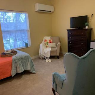 A cozy bedroom with a bed, armchair, dresser, and TV.