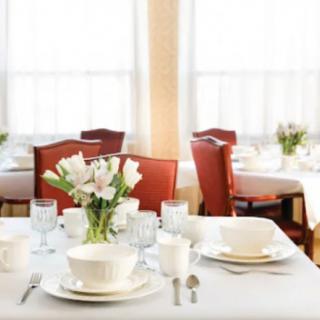 A beautifully set dining table with a white tablecloth, adorned with flowers and complete with plates, glasses, and cutlery.