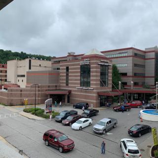 A view of a modern hospital complex with a bustling parking lot under a cloudy sky.