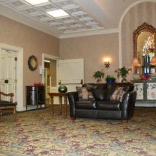 A warmly decorated lobby area with a sofa, mirror, plants, and intricate carpeting.