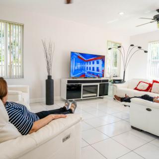 A modern living room with people relaxing on white sofas, watching television.