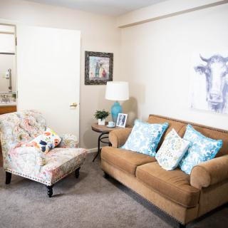 A cozy living room with a brown sofa and floral armchair, accented by decorative pillows and artwork.
