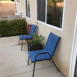 Two blue chairs on a patio next to windows with surrounding greenery.