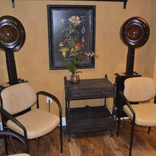 A cozy salon waiting area with chairs and hair dryers, featuring a floral painting on the wall.