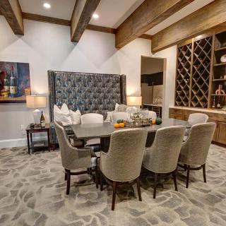 A luxurious dining room with a large table, upholstered chairs, and wine storage.