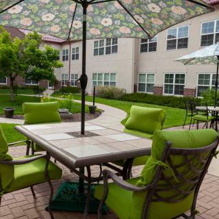 An inviting outdoor patio with green-cushioned chairs and floral umbrellas in a residential courtyard.