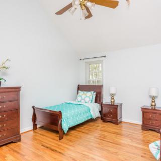 A simple bedroom with wooden furniture, including a bed, nightstands, and a dresser, featuring hardwood floors and a ceiling fan.
