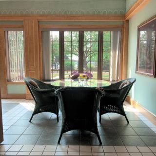 A cozy dining area with a round table surrounded by four chairs, bathed in natural light from large windows.