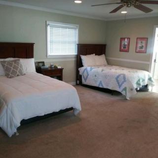 A spacious bedroom with two neatly made beds, a window, and ceiling fan.