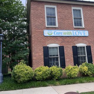 A brick building featuring a sign that reads 'Currents of Love' surrounded by lush greenery.