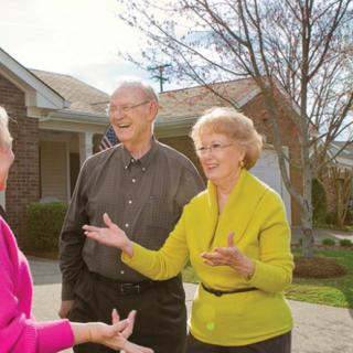 A group of seniors enjoy a conversation outdoors in a residential neighborhood.